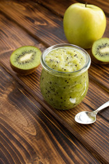 Smoothies or puree  with kiwi  and apple  in the small glass jar on the brown wooden  background.  Location vertical.