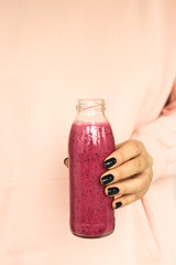Smoothies with berries in a bottle with a metal straw in female hands.