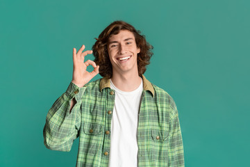 Happy Caucasian guy showing OK gesture on turquoise background