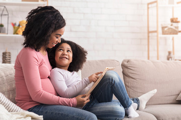 Little Black Girl Reading Book With Her Pregnant Mom At Home