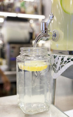 Lemonade dispenser filling a big jar with slice of lemon. Coffee shop background