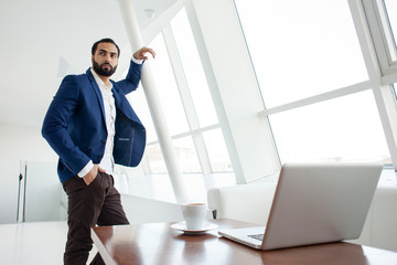 The head of the company stands in a white office and looks out the window, a successful businessman at a working place, an office worker in a large company