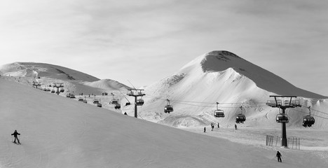 Panorama of snowy ski track prepared by snowcat, chair lift, skiers and snowboarders in ski resort