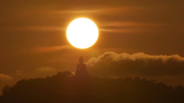 hue sunset over  silhouette Phuket big buddha statue on hilltop with many big trees high mountain, tourist photo spot in the beautiful evening colourful  orange twilight sky,moving cloud,flying bird