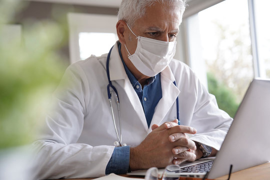 Doctor In Office Working On Laptop, Wearing Protection Mask