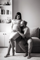 Fototapeta na wymiar Pregnancy. Young couple waiting for baby. Wonderful expectant parents cuddle in their apartment awaiting birth