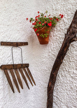 Fachada t&iacute;pica andaluza con una maceta con geranios colgada junto a aperos de labranza tradicionales