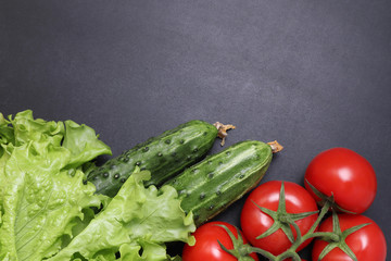 Green lettuce, red ripe tomatoes on a branch, fresh cucumbers and red bell peppers paprika. Vegetables on a black textured background.