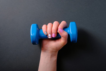 Girl holds a blue dumbbell in her hands, on a dark background