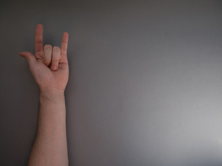Female hand shows a gesture of rock horns on gray background