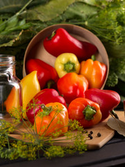 Nearby is a can, scattered with black peas. Juicy peppers on the background of a large fragrant bunch of dill and horseradish leaves. Vegetable preservation season.