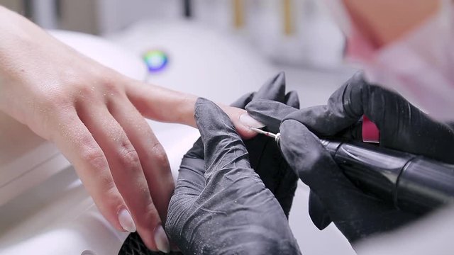 Woman manicurist with gloves in a beauty salon does a hardware manicure to a client before applying a gel coating