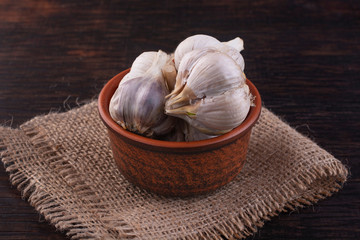 A few heads of garlic in a clay bowl on burlap close-up.