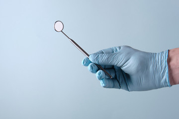 Dentist holds a mirror in his hand, on a blue background