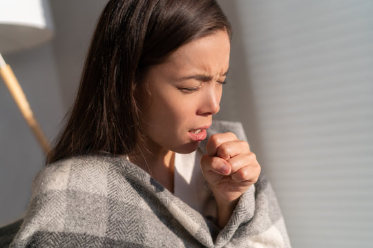 Asian woman coughing in fist sick of coronavirus viral infection spreading corona virus by not covering mouth and nose. Painful cough ill young chinese girl at home.