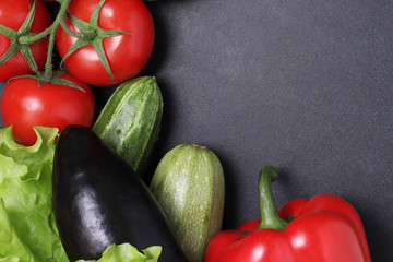 Green lettuce, red ripe tomatoes on a branch, fresh cucumbers and red bell peppers paprika. Vegetables on a black textured background.