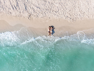 A couple in a swimsuit is lying on the shore of the azure sea in the sand shot from a quadrocopter