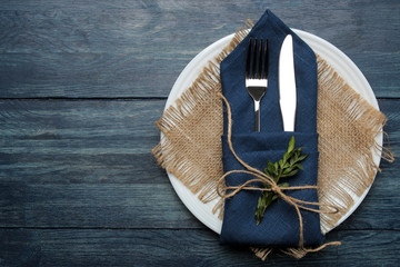 Table setting. plate and cutlery in a blue napkin, fork and knife on a blue wooden table. top view