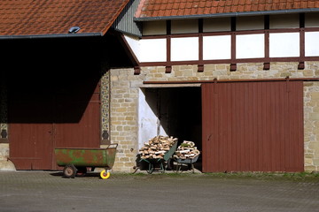 Schubkarren mit Brennholz in der Einfahrt einer Scheune mit Holztor und Fachwerk auf einem...