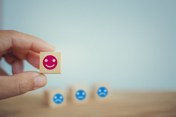 Satisfaction survey concept: Hand chooses a smiley face on wood block cube. depicts the best excellent business services rating customer experience.