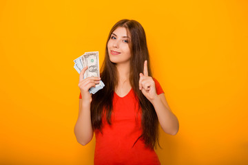 Attractive, young woman holds money notes in her hands, concept of savings and cashback. Studio photo on a yellow background.