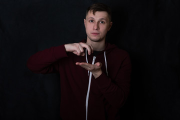 Studio portrait of a young man in a red sweatshirt against black background. A deaf-mute guy shows a 
