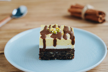  A piece of orange-chocolate cake. Spoon and cinnamon on a wooden background. Raw dessert with a nut base.
