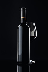 Bottle and glass of red wine on a black background.