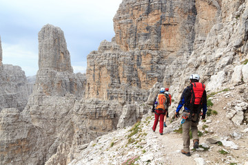 People hiking on via ferrata Sentiero delle Bocchette Centrale and mountain Campanile Basso in...