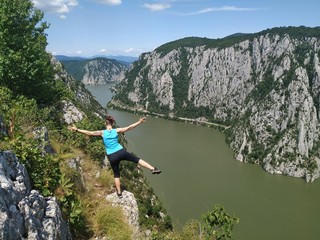 Girl standing on a rocky cliff hundred meters above the Danube Valley between Romania and Serbia, Yoga posing in the sun, meditating with arms wide open 