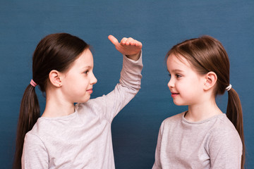 Two girls sisters compare each other's growth with a palm on a blue background