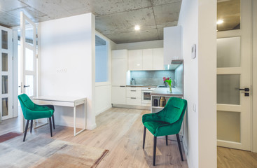 Fototapeta na wymiar Modern interior of living room and kitchen in new studio apartment. Green chairs. White kitchen.