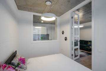 Modern contemporary interior of bedroom. Cozy bed. Window to the kitchen. Door to the living room.