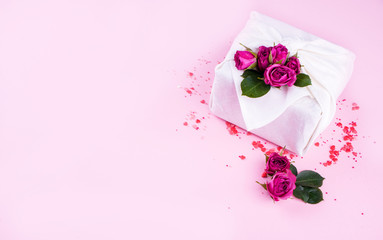 The gift is packed in the style of furoshiki, with hearts and flowers on a pink background. A Valentine's Day gift.