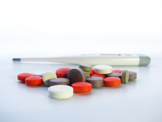 multicolored tablets and a thermometer on a light background