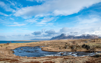 River surrounded by grass tundra in Iceland with snowcapped mountains and the sea in the background