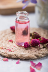 Obraz na płótnie Canvas Natural pure rose oil or scented water in bottles for spa, skin care or aromatherapy with pink roses dry. Organic cosmetics concept. Selective focus