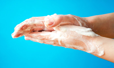 Fototapeta premium Women's hands are holding soap. Soap foam on the hands. Yellow soap in the hands. Woman washes soap with hands side view on a blue background. Virus protection. COVID-19