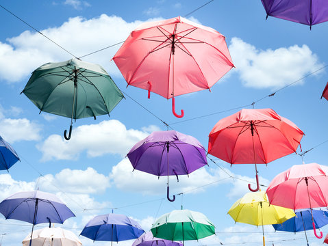 Multicolor parasol umbrella float in open air with sunny bright blue sky and white clouds ornament installation design for summer festival about happiness and freedom idea conceptual art