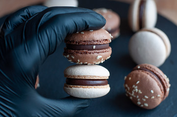 Hand in black gloves holds two macarons with chocolate ganache and sesame seeds