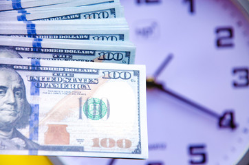 Analog white clock and dollars on a gray, yellow, blue background. Banknotes next to the clock, on top. Place for text.  Business, are you ready? Copy Space