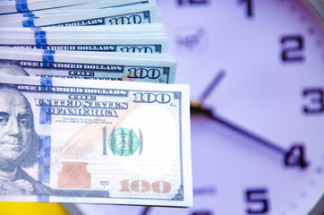 Fototapeta premium Analog white clock and dollars on a gray, yellow, blue background. Banknotes next to the clock, on top. Place for text. Business, are you ready? Copy Space