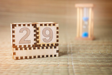 Calendar, wooden cube with date 29 and an empty space for the month, on an abstract woven hourglass background.