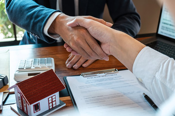 Real estate agent are shaking hands after good deal and giving house, keys to customer after...