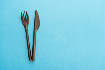 black plastic fork and knife on a blue background, top view, selective focus