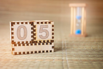 Calendar, wooden cube with date 5 and an empty space for the month, on an abstract woven hourglass...