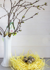 Easter composition with a bouquet of birch branches in a vase and quail eggs on a white wooden background.