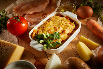 Close up of vegetable casserole with cheese salmo, chicken on kitchen table. Flatlay of salmo pudding (pie) on wooden background. Rustic homemade casserole. Healthy vegetarian cuisine.