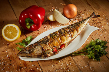 Appetizing grilled fish with vegetables on wooden background. Homemade smoked mackerel fish. Appetizing scomber prepared on tandoor (barbecue) on a brown rustic wooden table.