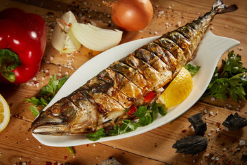 Appetizing grilled fish with vegetables on wooden background. Homemade smoked mackerel fish....